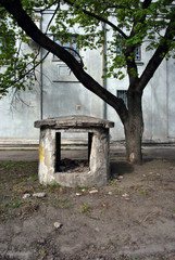 An old ventilation building destroyed, disabled made of concrete, with a warning on a yellow background: do not dig, an electrical cable at a shallow depth; near acer tree and old gray house wall