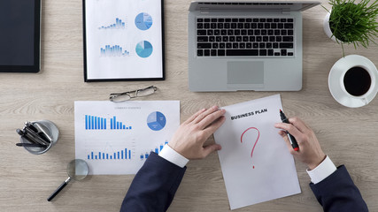 Business person drawing question mark on business plan, lack of ideas, top view