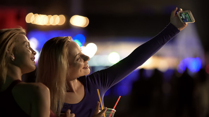Beautiful female friends posing for selfie on smartphone, having fun at party