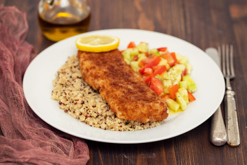 fried fish with salad, qiuinoa and lemon on white plate