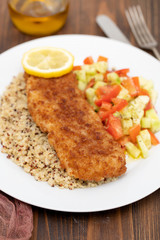 fried fish with salad, qiuinoa and lemon on white plate