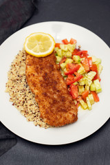 fried fish with salad, qiuinoa and lemon on white plate
