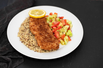 fried fish with salad, qiuinoa and lemon on white plate