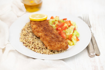 fried fish with salad, qiuinoa and lemon on white plate