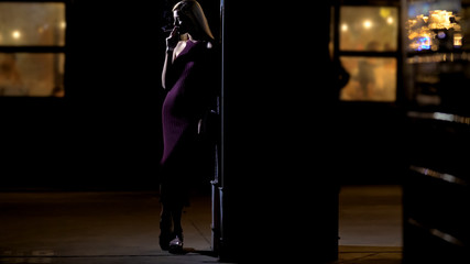 Lonely blond lady enjoying cigarette smoke while standing alone near night club