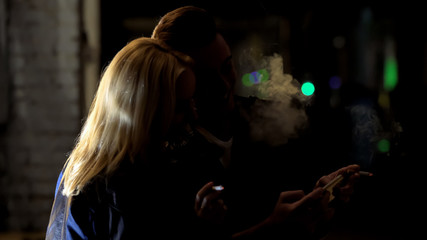 Young couple smoking cigarettes and viewing photos on smartphone together