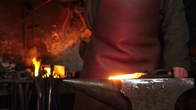 The hands of smith beat on glowing hot metal and sparks fly in all directions