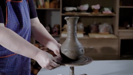 potter is wearing an apron is putting new fresh clay bowl on a rotating platform in working studio, demonstrating product