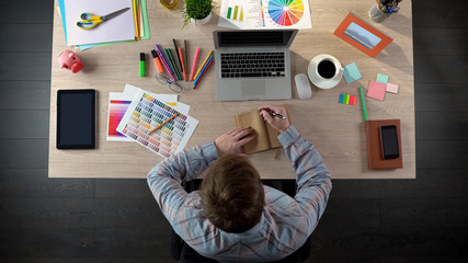 Male designer making notes in his notebook to discuss them with client, top view