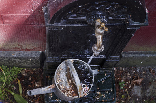 Water tap filling old watering can
