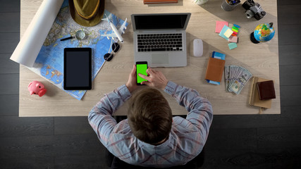 Man swiping pages on smartphone with green screen, using travel application