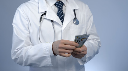 Male doctor counting money, paid health care services at private clinic, bribe