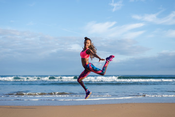 Sporty brazilian woman dancing and jumping at the beach. Black happy dancer practicing dance jumps and having fun outdoor.