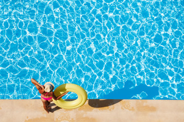 Fototapeta na wymiar Woman in straw hat at poolside with rubber ring