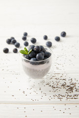 close up view of sweet chia seed pudding with blueberries and mint on white wooden surface