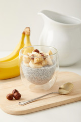close up view of chia seed pudding with pieces of banana and hazelnuts on wooden cutting board with spoon