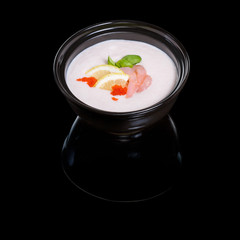 Creamy soup with shrimp in a black bowl on the black background with reflection