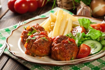 Roasted meatballs in tomato sauce with french fries and salad