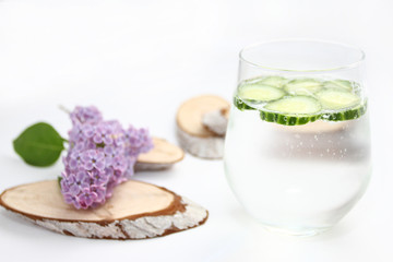 Detox flavored water with cucumber on white background with lilac and wood decoration. Healthy food concept.  Refreshing summer homemade cocktail. Copy space. 