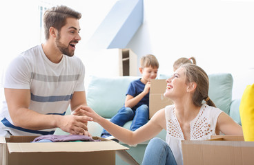 Young couple packing boxes with their children indoors. Happy family on moving day