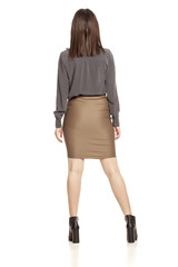 Back view of young businesswoman in skirt, shirt and boots standing on white background