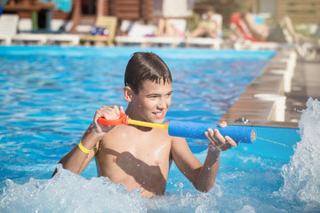 The child plays in the pool with a water gun in sunny weather