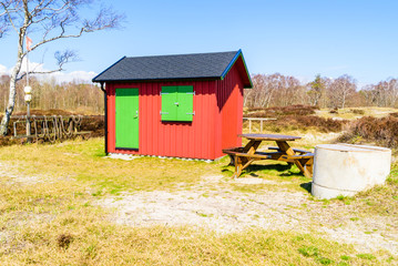 Hagestad nature reserve in Loderup, Sweden - Small red shed with green doors beside an outdoor bench and fireplace.