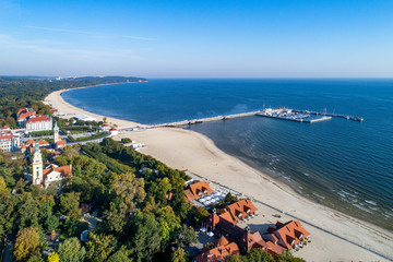 Sopot resort in Poland. Wooden pier (molo) with marina, yachts, beach, old lighthouse, church, vacation infrastructure, hotels, park and promenade. Far view of Gdynia.  Aerial view at sunrise