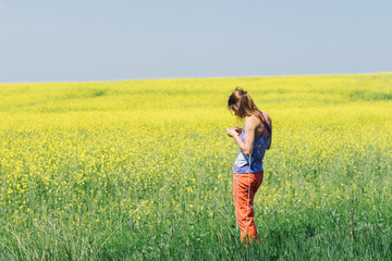 Smiling girl stands in the field of yellow flowers and look into the sky