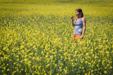 Smiling girl stands in the field of yellow flowers and look into the sky