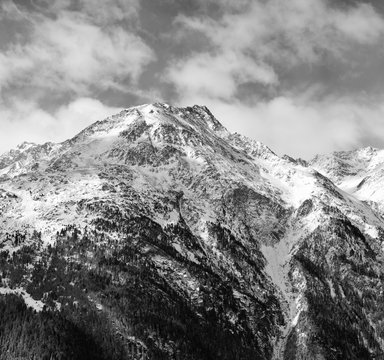 Fototapeta Black-and-white Alpine landscape. High mountain covered with snow on a background cloudy sky