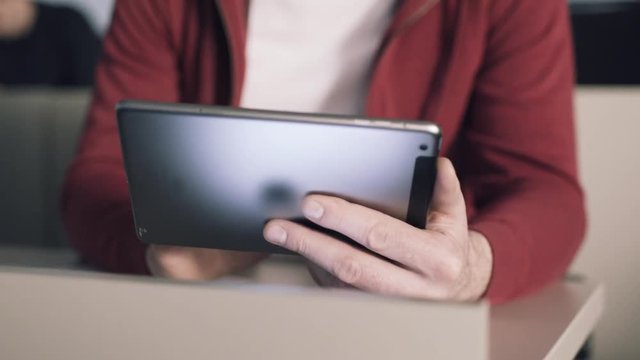 Young student sitting at desk interact with tablet computer and reads books. Stock. Education. University