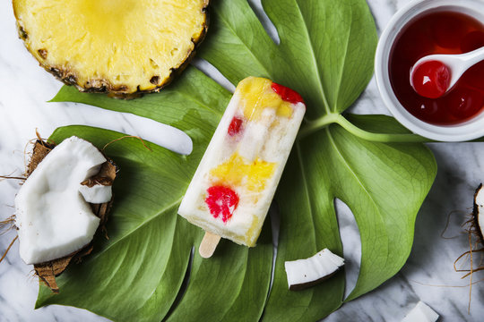 Pina Colada popsicle with candied cherries and pineapple on leaf
