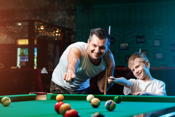 Father and son play billiards. The father teaches his son to play billiards. The concept of parents and children, upbringing, family rest.