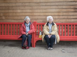 Two senior woman sitting and waiting on a red bench outdoors 