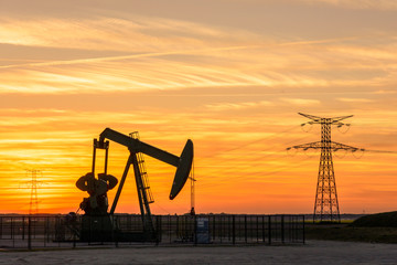 Pumpjack and transmission towers at sunset symbolizing energy transition. A pump jack pumping oil...