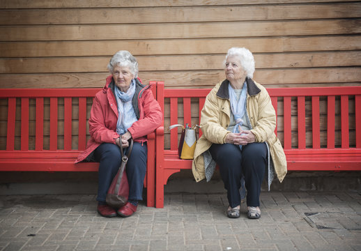 Two Happy Senior Women Sitting On A Red Bench Outdoors 