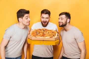 Three young happy men smelling a big pizza