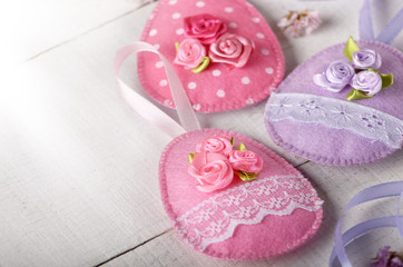 Handmade patchwork pink and lilac felt easter eggs on white wooden table