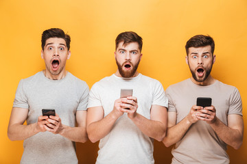 Three young shocked men holding mobile phones