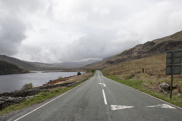An empty long road surrounded by green hills and mountains 