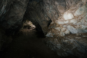Beautiful cave. View from inside dark dungeon. Textured walls of cave. Background image of underground. Dampness inside cave. Light at end of tunnel.