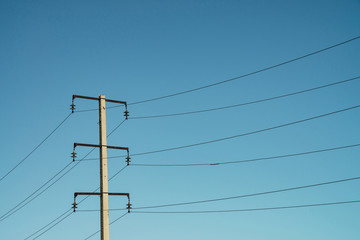 Posts with wires of high voltage on background of blue sky in sunlight. Background image of many...