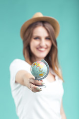 Smiling blonde girl wears white t-shirt and hat holding small globe on blue background