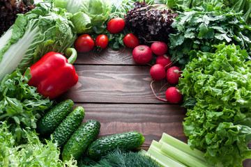 wreath of green lettuce leaves and red vegetables lying in a circle with space for text