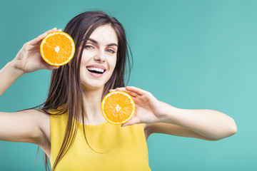 Portrait of beautiful brunette smiling girl holding two cutted orange fruit parts near her face before colorful background, healthy freshness concept