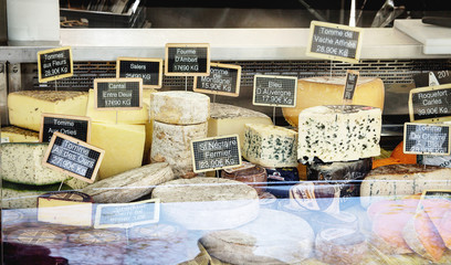 Market stall with fresh cheese assortment at Parisian street farmers market. White asparagus, tomatoes, cucumbers.