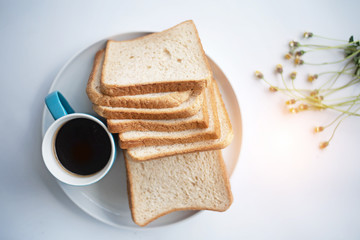 Fototapeta na wymiar The blue ceramic coffee cup with black coffee put beside sliced bread,on white table,blurry light around.