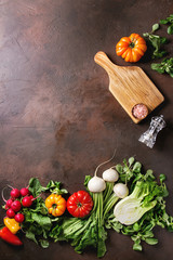 Variety of wet raw fresh organic colorful vegetables tomatoes, radish with leaves, fennel, paprika, salt, pepper, wooden chopping board for salad over dark brown texture background. Top view, space.