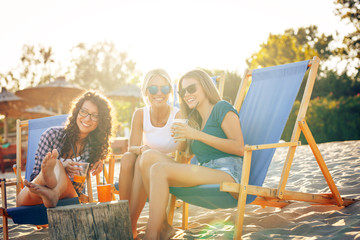 Group of young casual female friends sitting on beach on sun beds,hangout and relaxing.